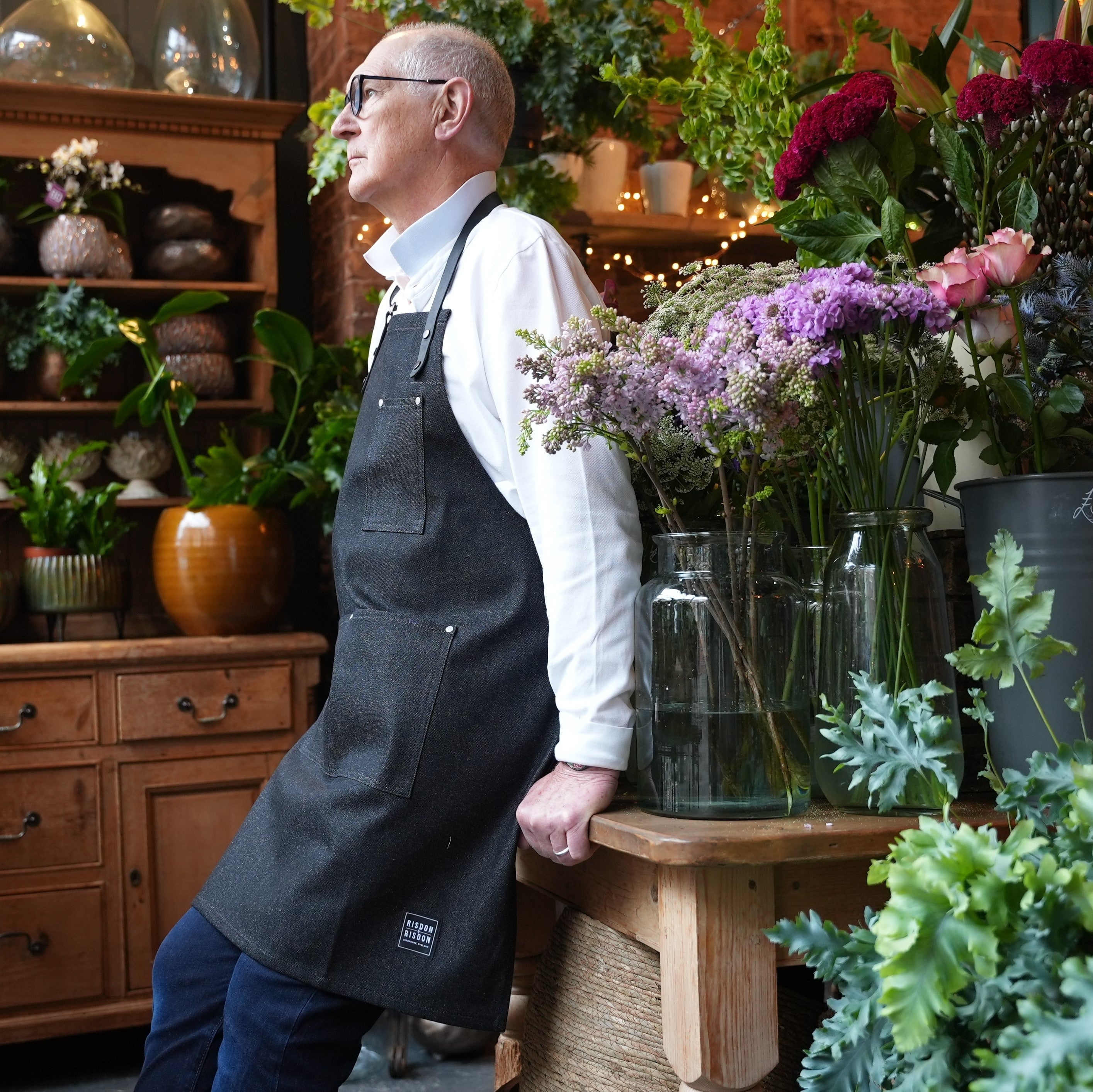 Male florist wearing handcrafted, black denim apron with removable straps; made in Britain.
